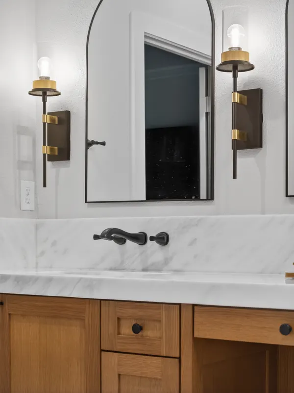 Arched black mirror between black and brass sconces, over a marble-look vanity top