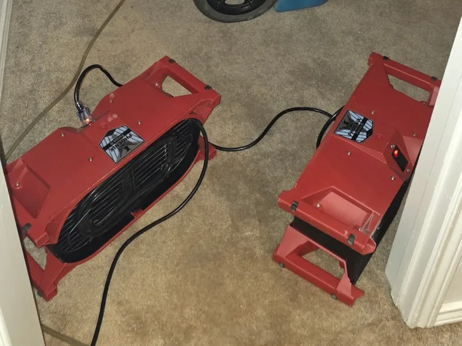 Two air movers drying a carpeted hallway outside a laundry closet after water damage