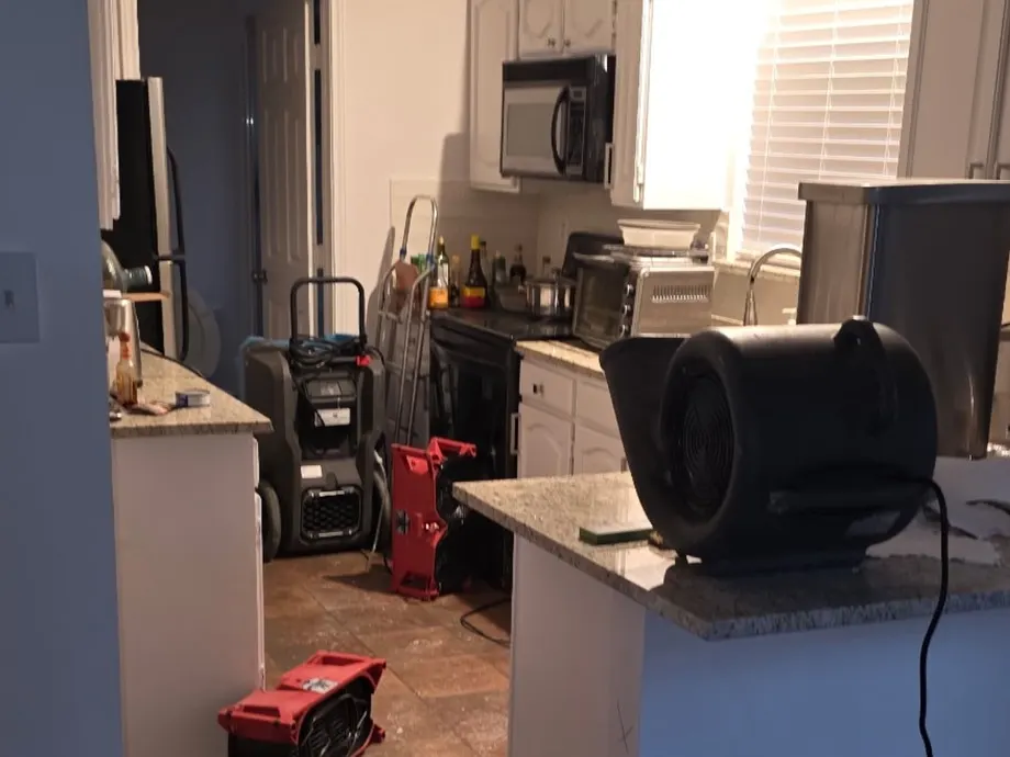 Kitchen during a water damage dry-out: air movers on the tile floor, a fan on the granite counter and a dehumidifier by the fridge
